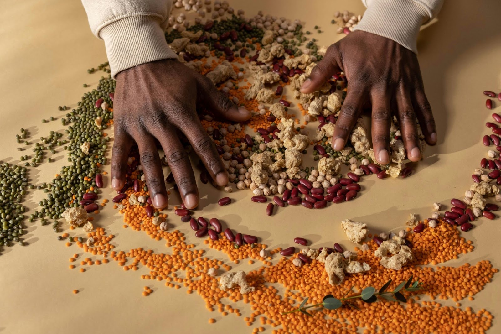 Hands spreading a variety of legumes over a table.